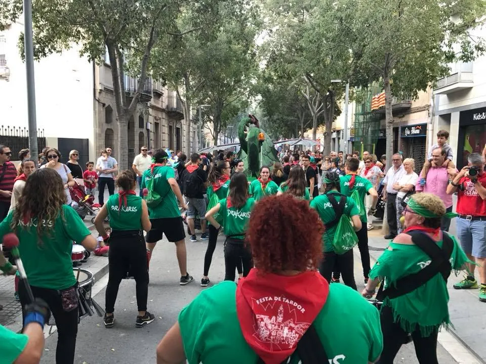 La colla, amb samarretes verdes i mocadors de la Festa de Tardor, tocant en una cercavila amb el Drac de Sant Feliu al fons